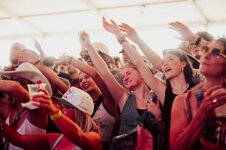 Festival crowd with hands raised under a tent at Bourbon & Beyond