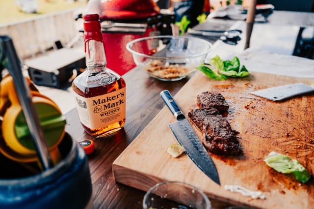 Maker's Mark bourbon bottle next to a grilled steak on a cutting board